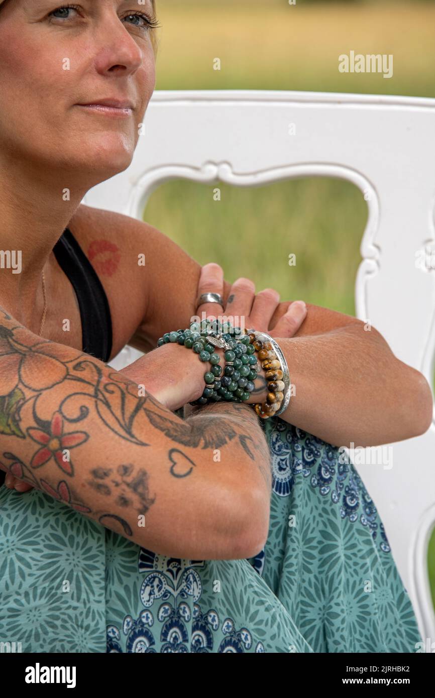 Parte del corpo di una donna europea di siiting con tatuaggi e piercing guardando lontano Foto Stock
