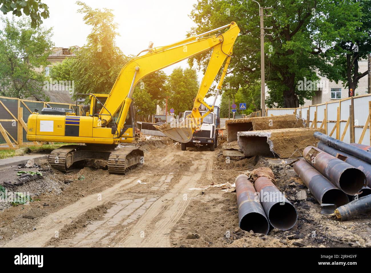 Un escavatore in un cantiere, vicino a tubi metallici, materiali da costruzione e macchinari. Concetto di costruzione Foto Stock