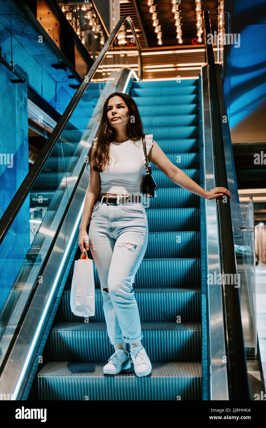 Giovane brunetta Latina attraente donna con borse per la spesa su scala mobile nel centro commerciale della moda. Foto Stock
