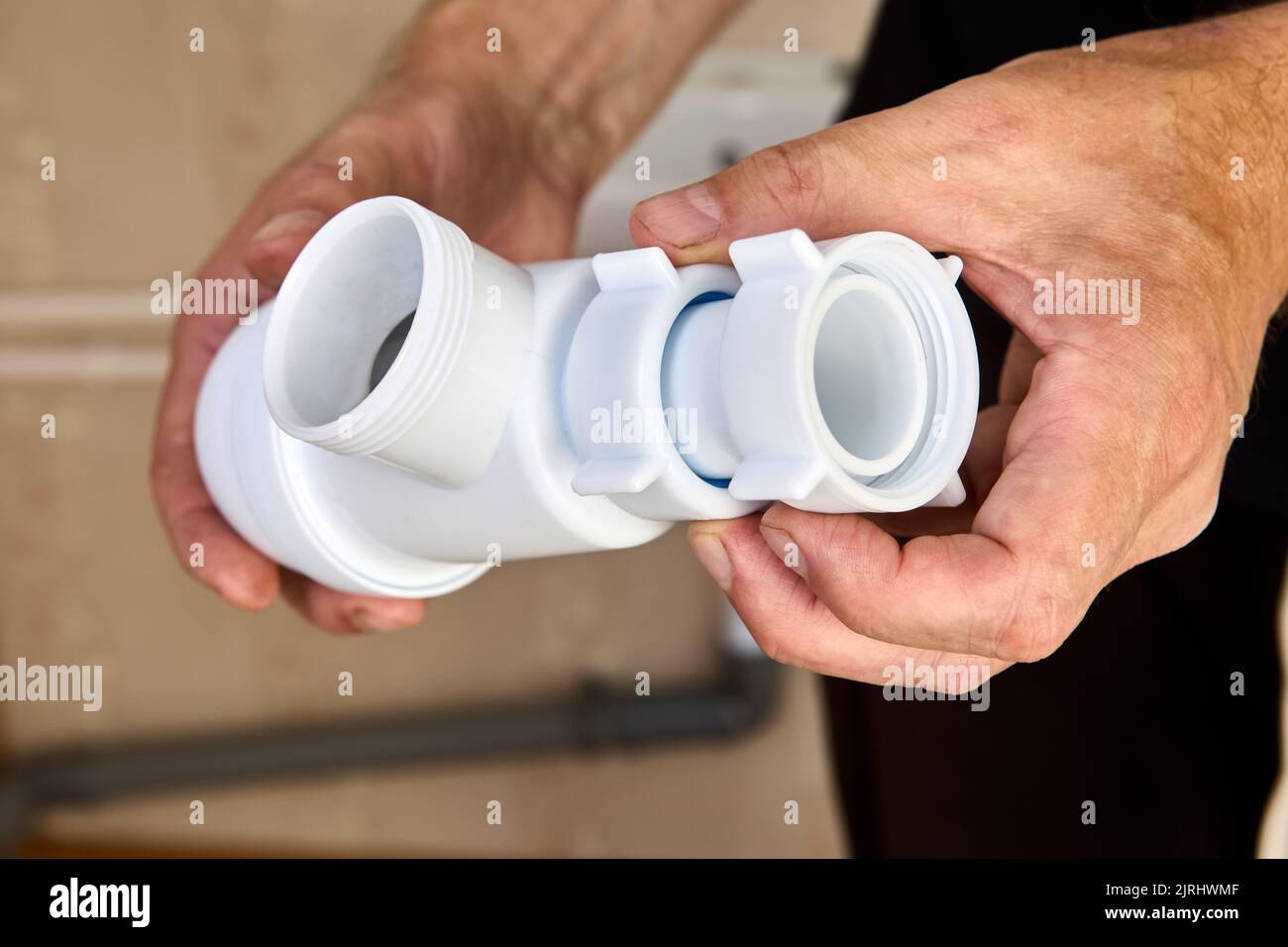 L'idraulico ispeziona le perdite di sifone di plastica dallo scarico del lavandino nel bagno. Foto Stock