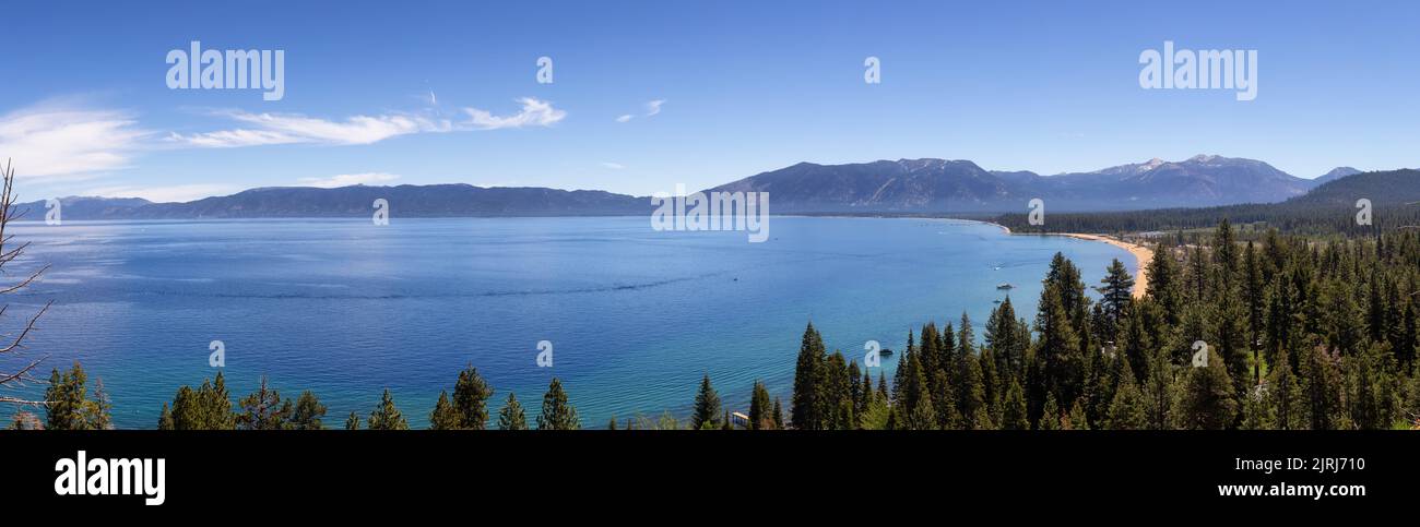 Vista panoramica del grande lago con spiaggia circondata da alberi e montagne. Foto Stock