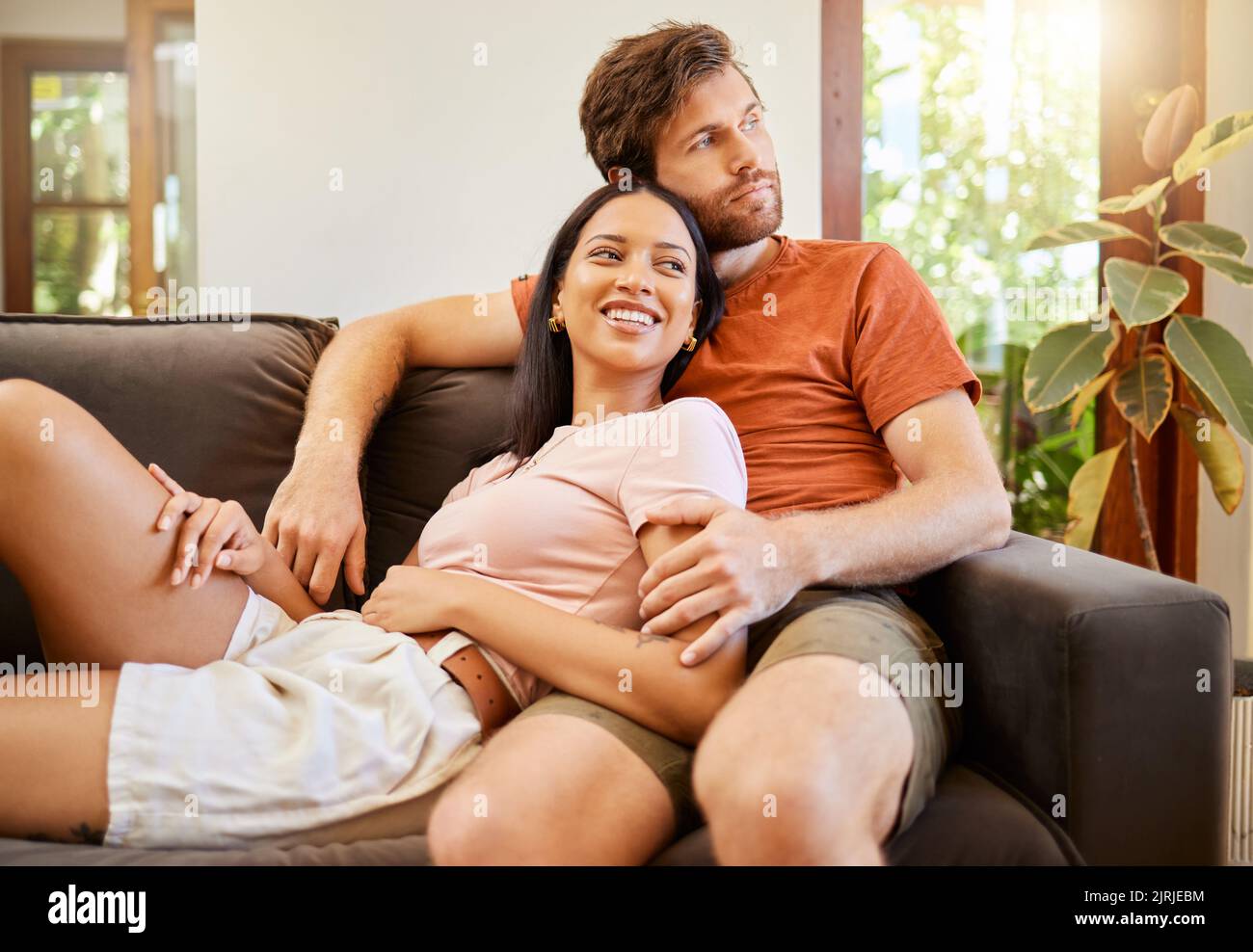 Felice, amore e coppia interrazziale sorriso guardando via relax e sedersi su un divano a casa. Diversità uomo e donna sorridendo e godendo la qualità Foto Stock