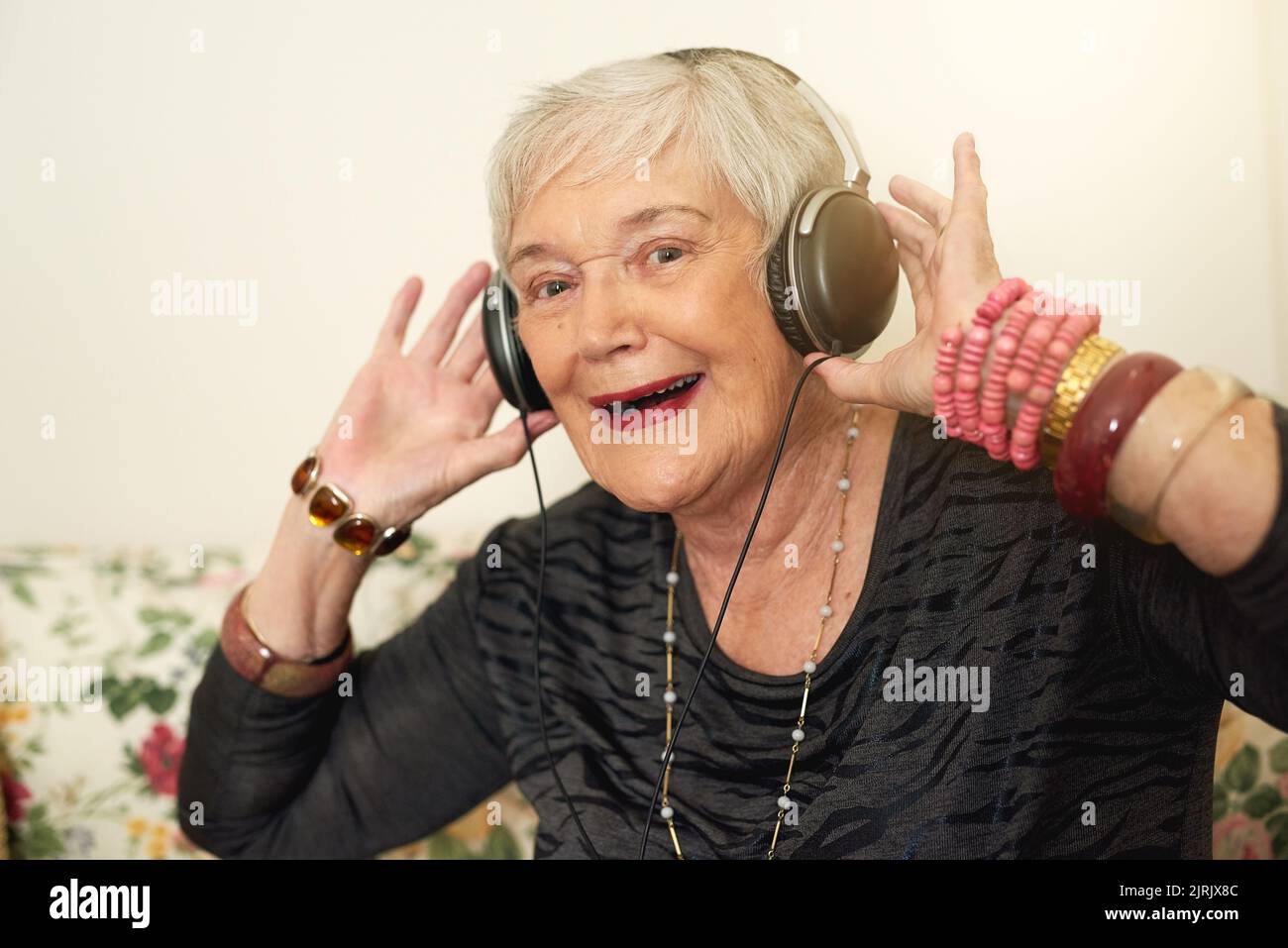 Questo anziano gode di un diverso tipo di marmellata. Ritratto di una donna anziana felice che usa le cuffie per ascoltare la musica nel suo salotto a casa. Foto Stock