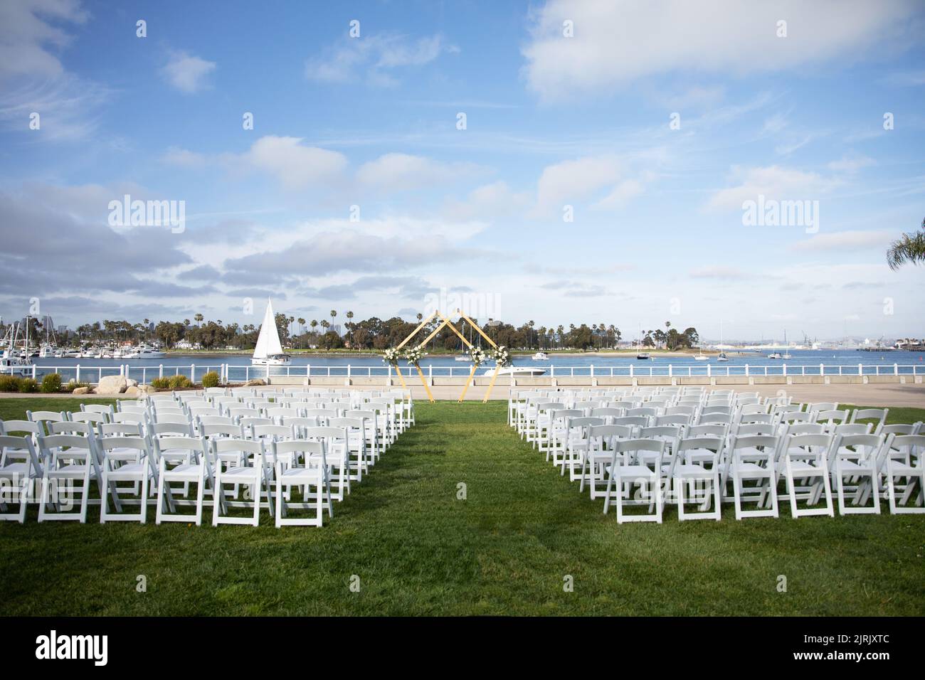 Matrimonio rombo doppio arco con rose bianche e foglie di eucalipto decorazione floreale. Cerimonia di matrimonio all'aperto con vista sulla baia e palme. Foto Stock