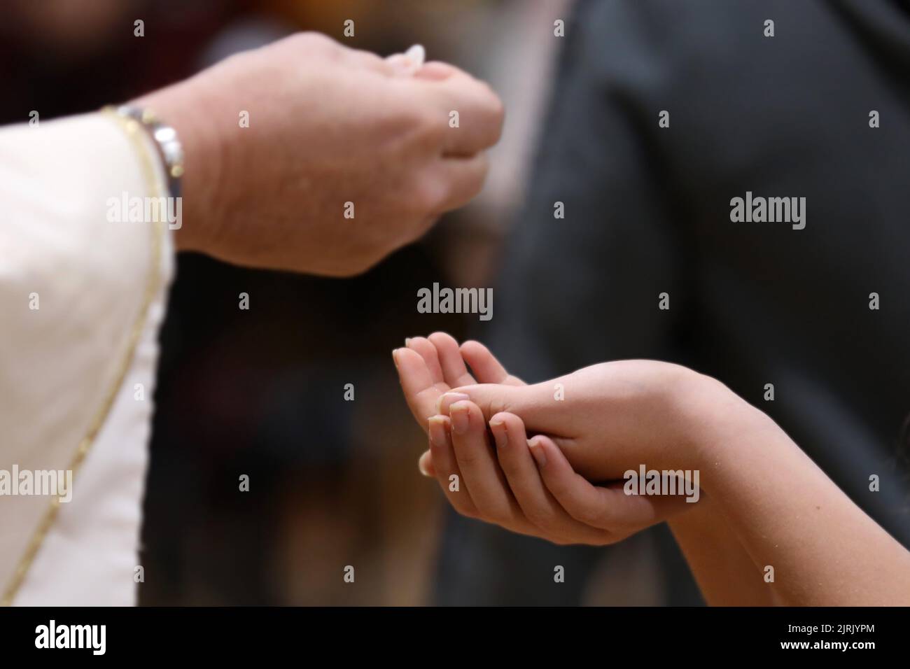 Le mani di un parrocchiano si sono unite per ricevere l'ostia o il pane da un sacerdote ad una messa cattolico o ad una liturgia o messa di comunione. Foto Stock