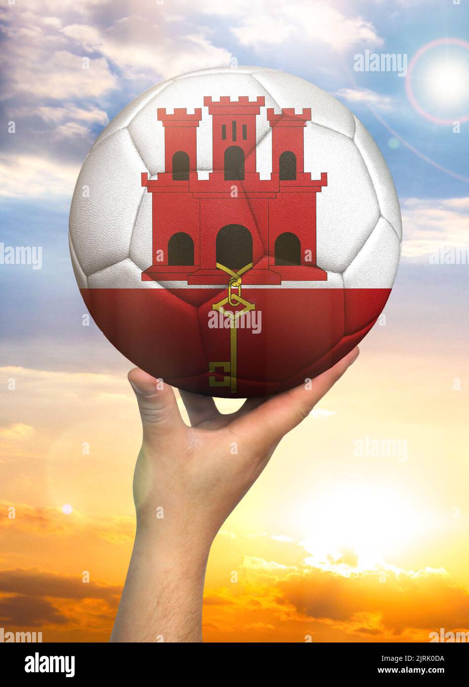 Pallone da calcio in mano con una rappresentazione della bandiera di Gibilterra contro un cielo colorato Foto Stock