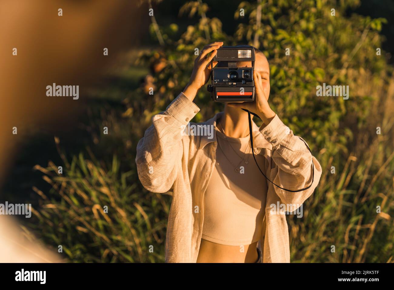 Una giovane ragazza che scatta foto della sua amica con una fotocamera vintage istantanea. Fine settimana in natura al tramonto d'estate . Foto di alta qualità Foto Stock