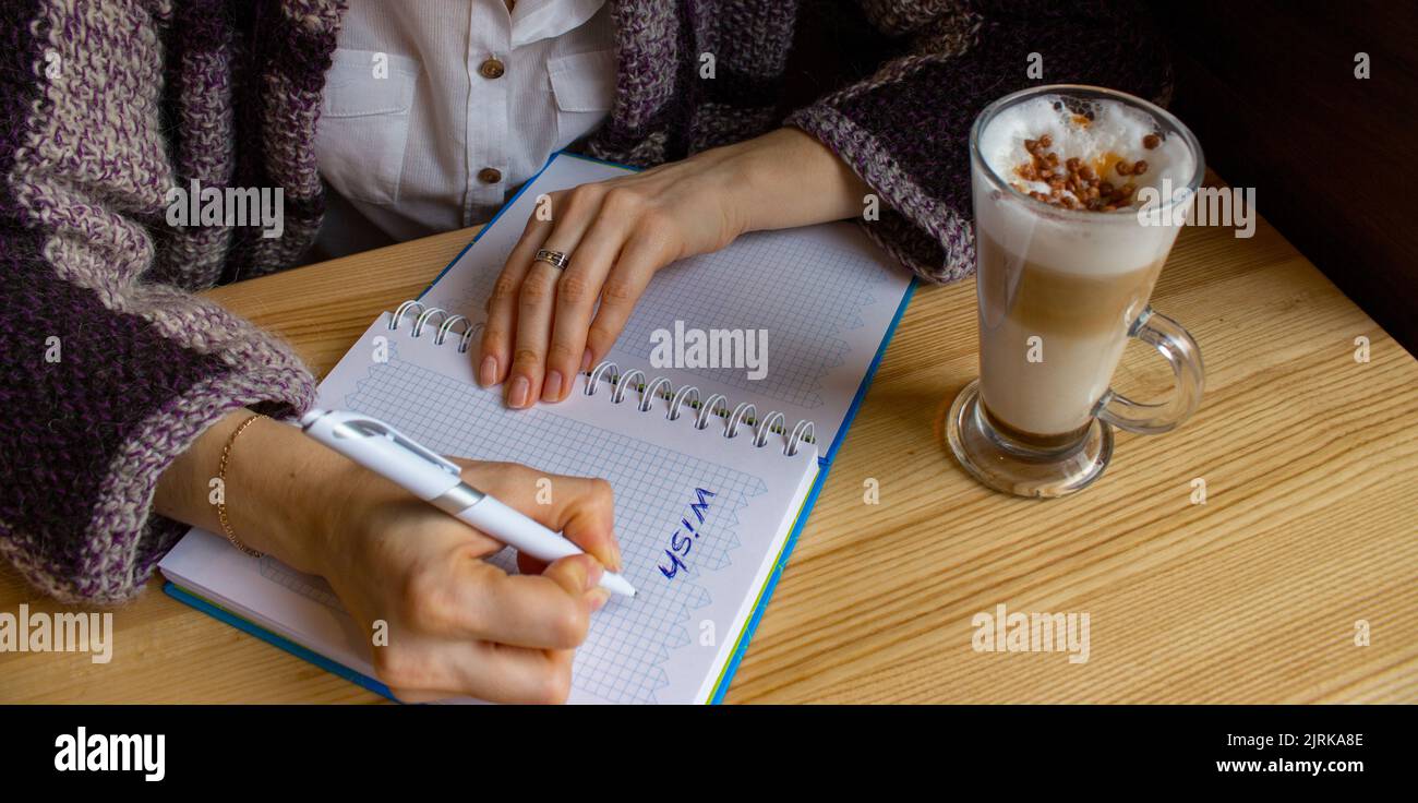 Ragazza che tiene la penna e scrivere la lista dei desideri. Pianificare il futuro con il notebook. Ragazza con lista dei desideri in caffè con latte. Ora del mattino per te. Foto Stock
