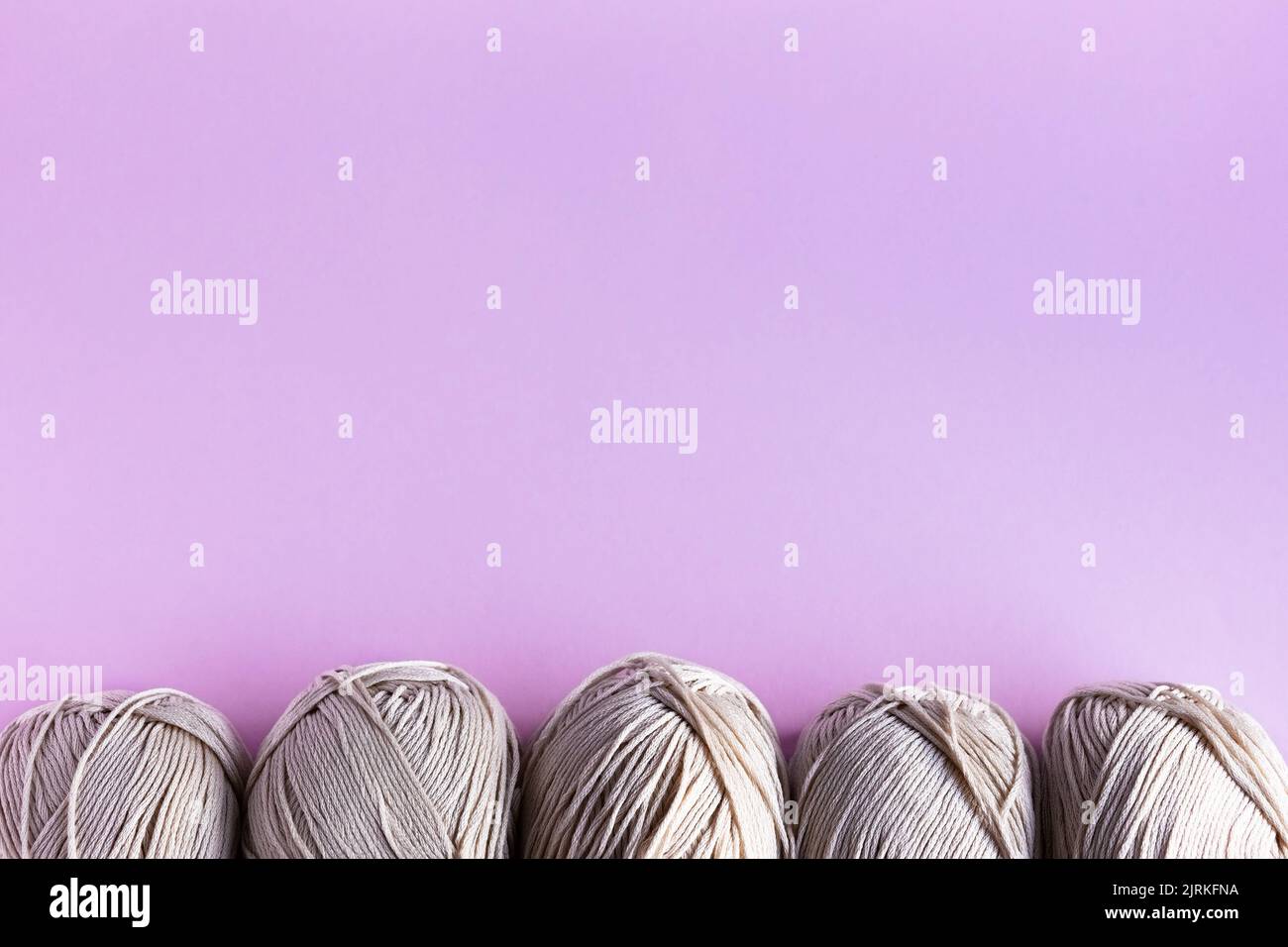 Fili in filo beige su fondo lilla per la lavorazione a maglia. Giacitura piatta Foto Stock
