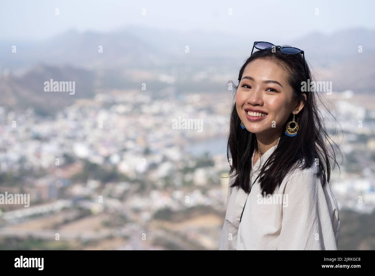 Felice femmina etnica sorridendo e guardando la macchina fotografica mentre si trova in piedi su sfondo sfocato della città vecchia di Pushkar in Rajasthan, India Foto Stock