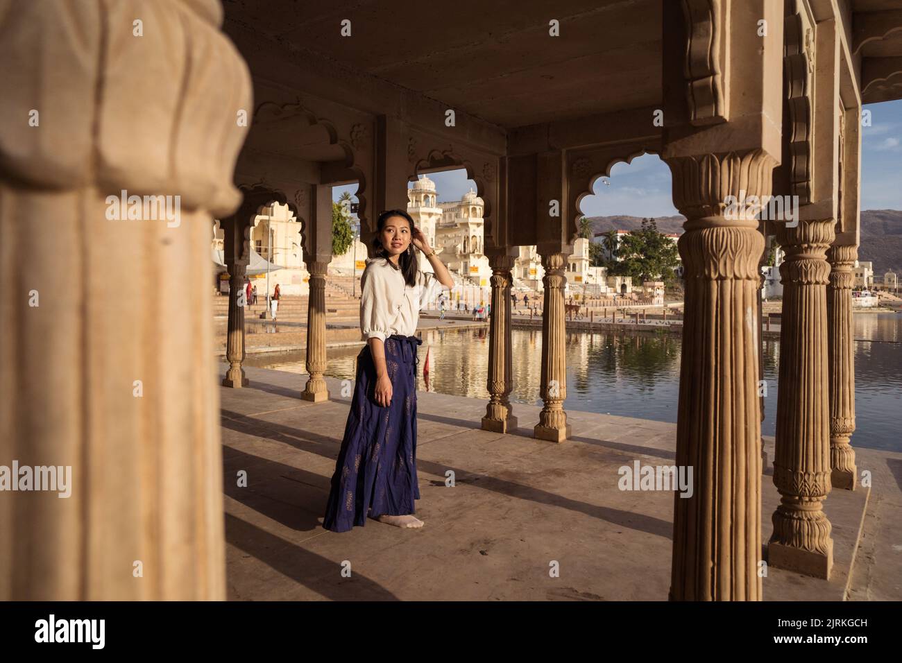 Corpo pieno donna asiatica guardando lontano mentre si trova sotto il tetto di edificio ad arco sulla costa del Lago Sacro Pushkar in Rajasthan, India Foto Stock