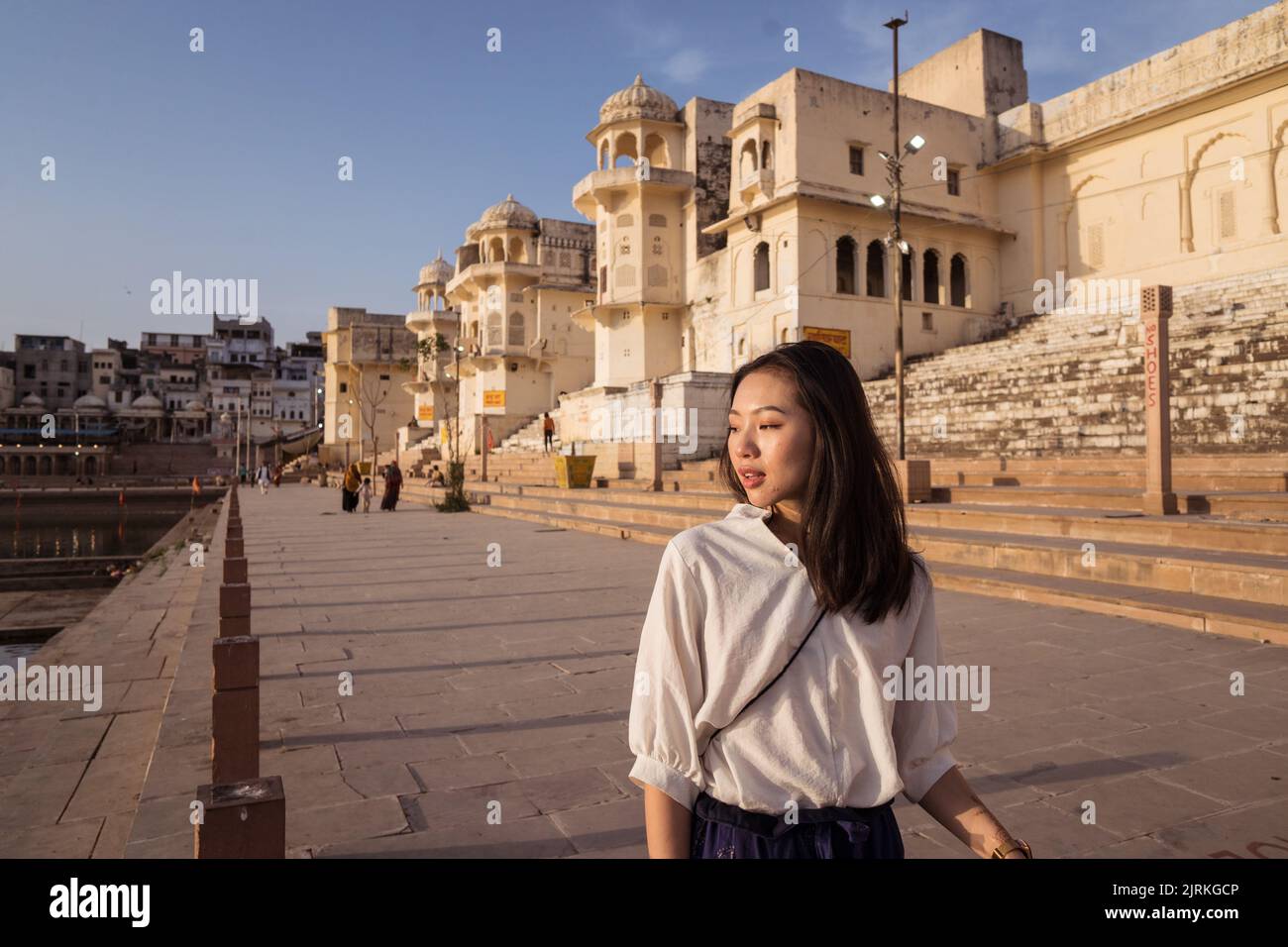 Donna etnica felice guardando via mentre camminando sulla riva lastricata del Lago Sacro Pushkar in giorno di sole in Rajasthan, India Foto Stock