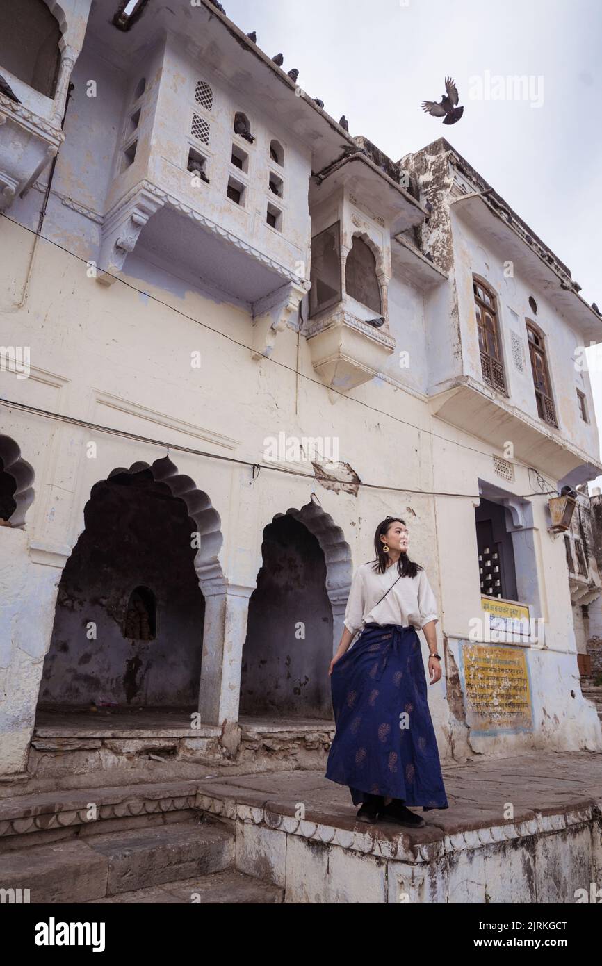 Basso angolo di etnia femminile in piedi contro il tempo vecchio edificio sulla riva del Lago Sacro Pushkar in Rajasthan, India Foto Stock
