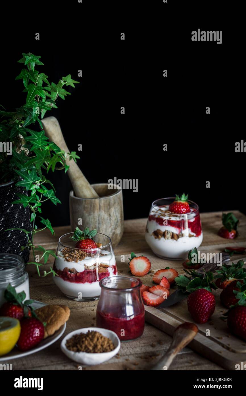 Alto angolo di dessert yummy con formaggio e fragola fresca matura in composizione in vaso di edera verde e mortaio invecchiato con pestello su tavola di legno contro Foto Stock