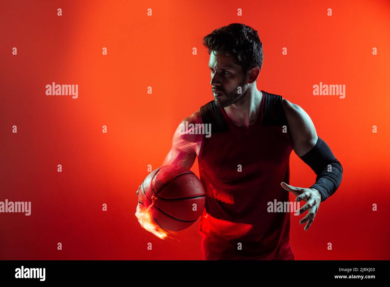Studio creativo girato di giocatore di basket in studio utilizzando gel colorati e luci proiettore e tenendo una palla in mano Foto Stock