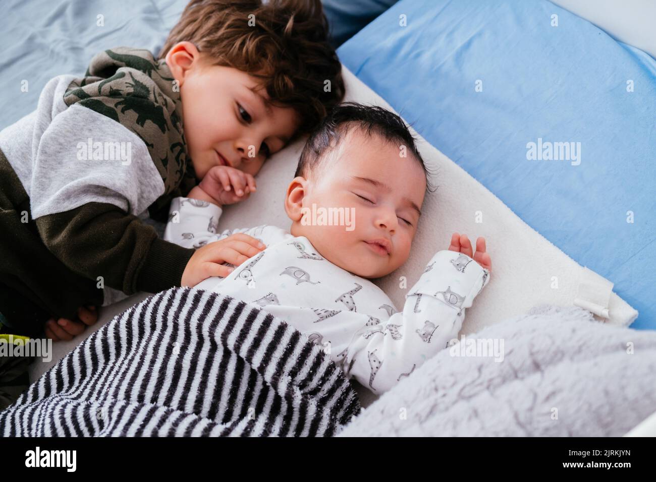 Dall'alto di un piccolo ragazzo affascinante abbracciare piccolo fratello mentre dormono pacificamente insieme in un comodo letto Foto Stock