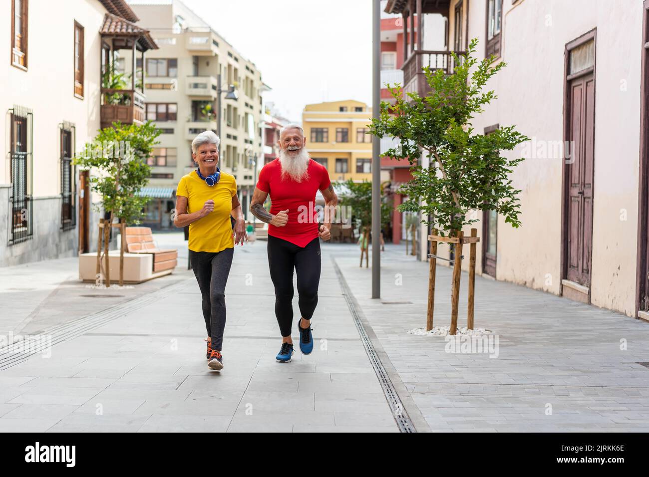 Vista frontale di una felice coppia senior che corre in città Foto Stock