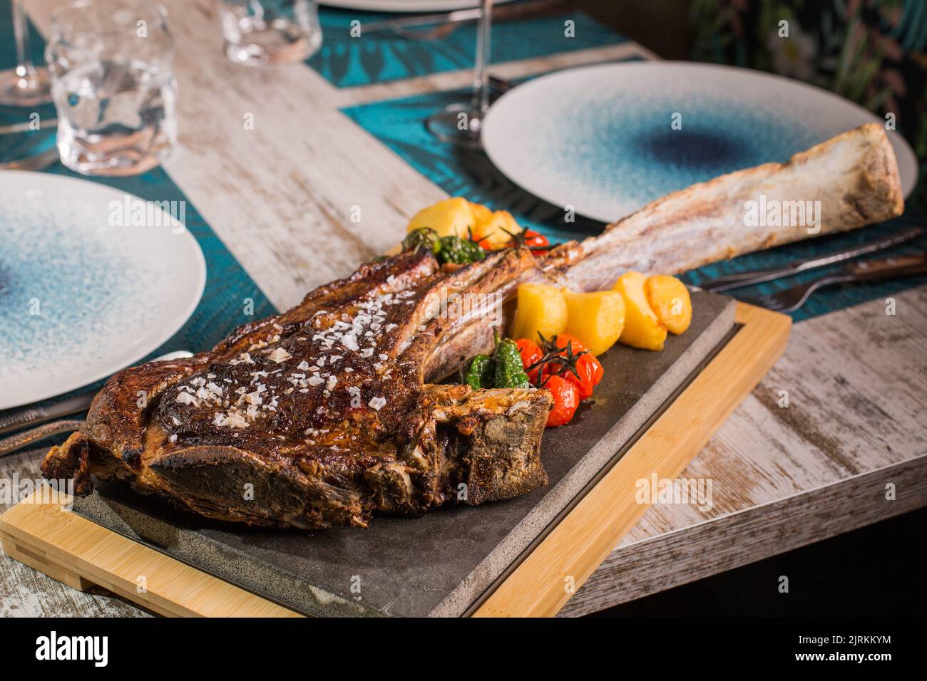Gustosa bistecca di manzo ribeye alla griglia con grani di sale e pomodori rossi e gialli luminosi sul tavolo servito Foto Stock