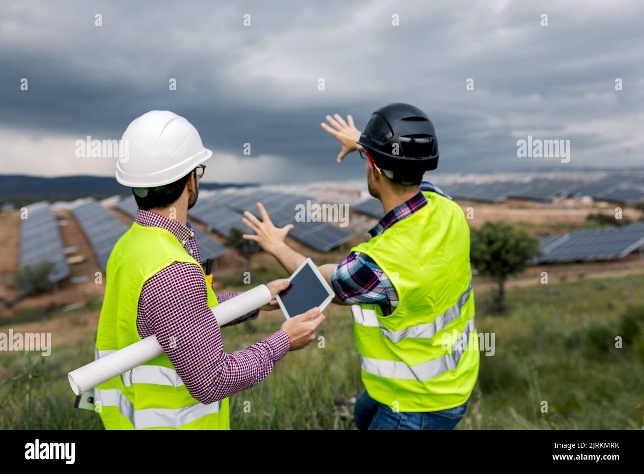 Anonimo uomo con tablet ascoltare gesticulating collega maschio mentre si discute di costruzione di centrale di energia solare il giorno overcast Foto Stock