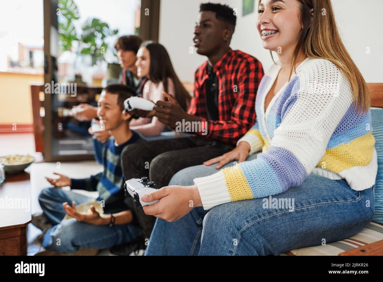 Giovani amici multirazziali che si divertono a giocare a videogiochi a casa - Focus sulla mano destra tenendo controller Foto Stock