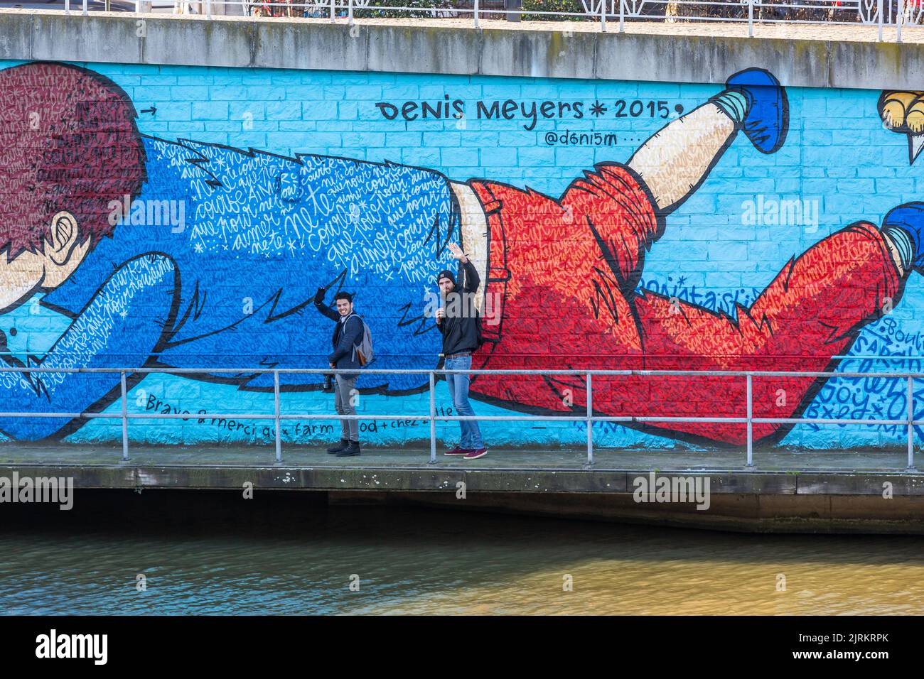 Due fotografi sventolano davanti a un murale sul bordo del canale a Bruxelles Foto Stock