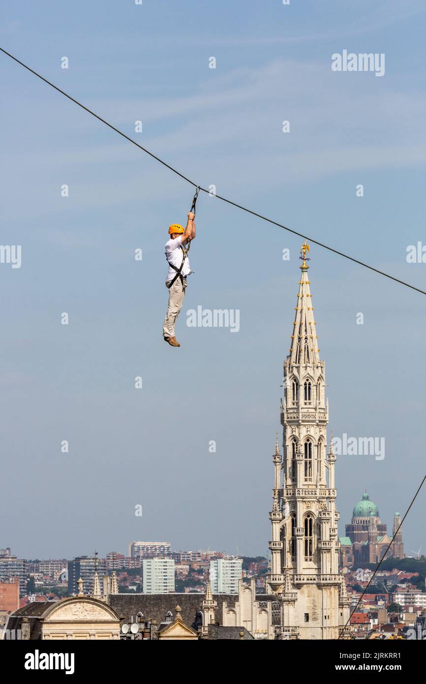Persona che pende da una corda davanti a una vista della torre del municipio di Bruxelles Foto Stock