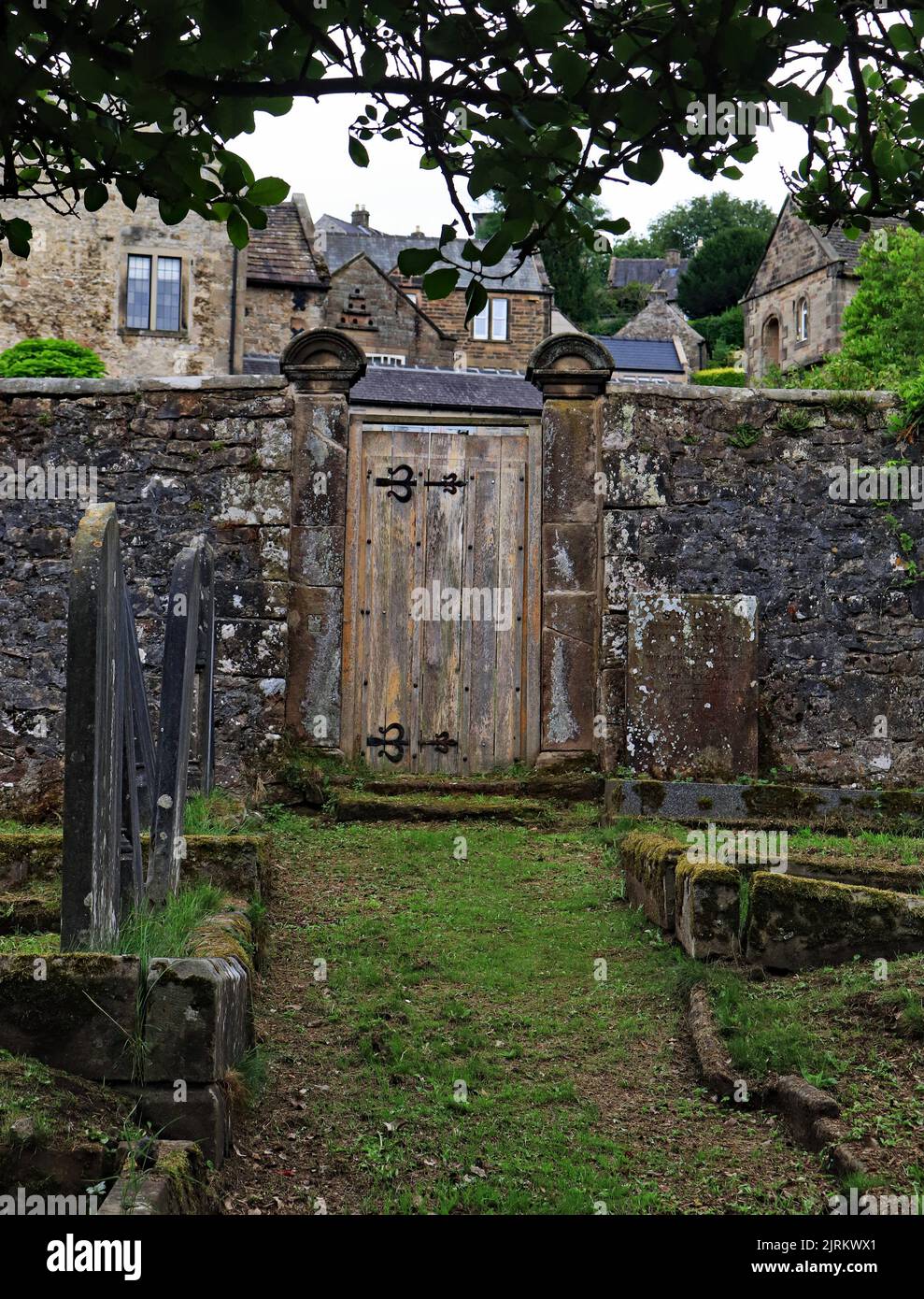 Un vecchio cancello di legno pesante nella parete intorno al cortile della chiesa di San Giovanni Battista nel pittoresco villaggio di Winster nel Derbyshire Foto Stock