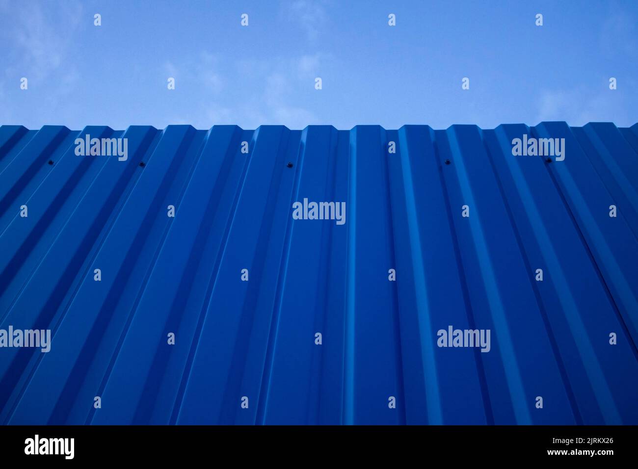 Struttura di una vecchia parete di recinzione scura dipinta di blu metallico con un cielo sullo sfondo. Foto Stock