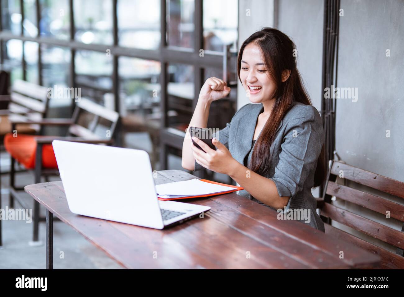 felice giovane donna d'affari eccitato mentre lavora e usando il suo telefono. Foto Stock