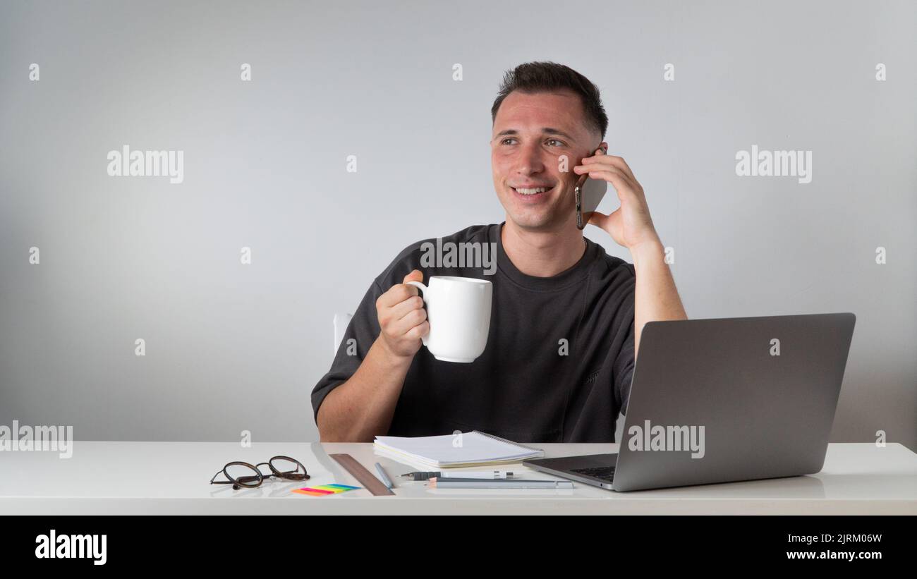 Uno studente di un notebook parla al telefono e beve un caffè, una pausa per riposarsi Foto Stock