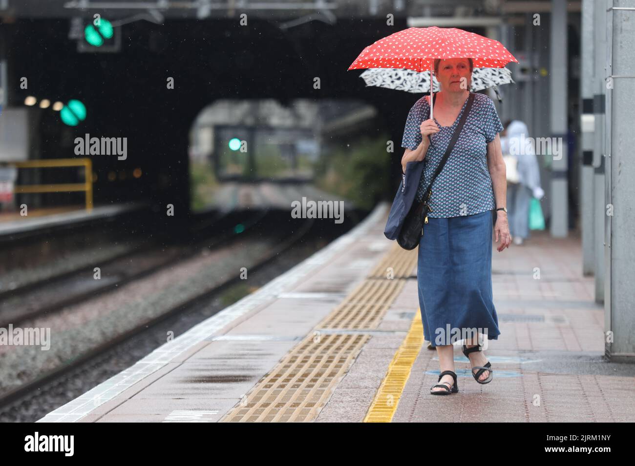 Una donna usa un ombrello mentre cammina lungo la piattaforma della stazione di Ealing Broadway, Londra occidentale, mentre il Met Office ha emesso un avvertimento giallo per temporali e forti piogge nel sud e nell'Inghilterra orientale, con condizioni di guida potenzialmente influenzate da spruzzi, acqua stagnante e persino grandine, oltre ai possibili ritardi nei servizi ferroviari, alle interruzioni dell'alimentazione, alle alluvioni e ai fulmini. Data immagine: Giovedì 25 agosto 2022. Foto Stock