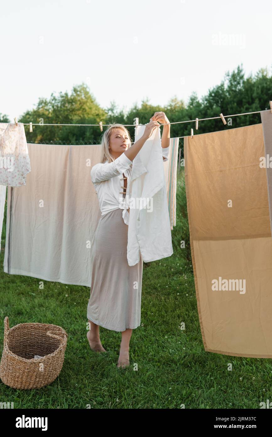 Lavanderia giorno. Una donna appende biancheria e asciugamani su un albero nel cortile di una casa di villaggio. Concetto di cottage estivo. Foto Stock