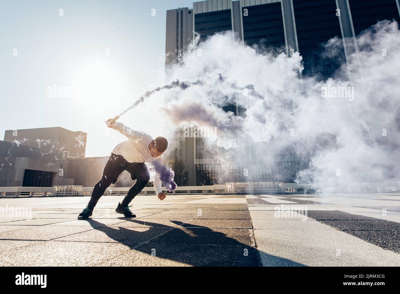 Uomo sportivo che pratica il parkour e la corsa libera facendo un flip con una granata di fumo. Free Runner in azione su sfondo urbano città. Foto Stock