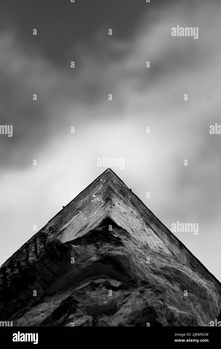 Uno scatto verticale di un angolo di parete di cemento contro un cielo cupo in scala di grigi Foto Stock