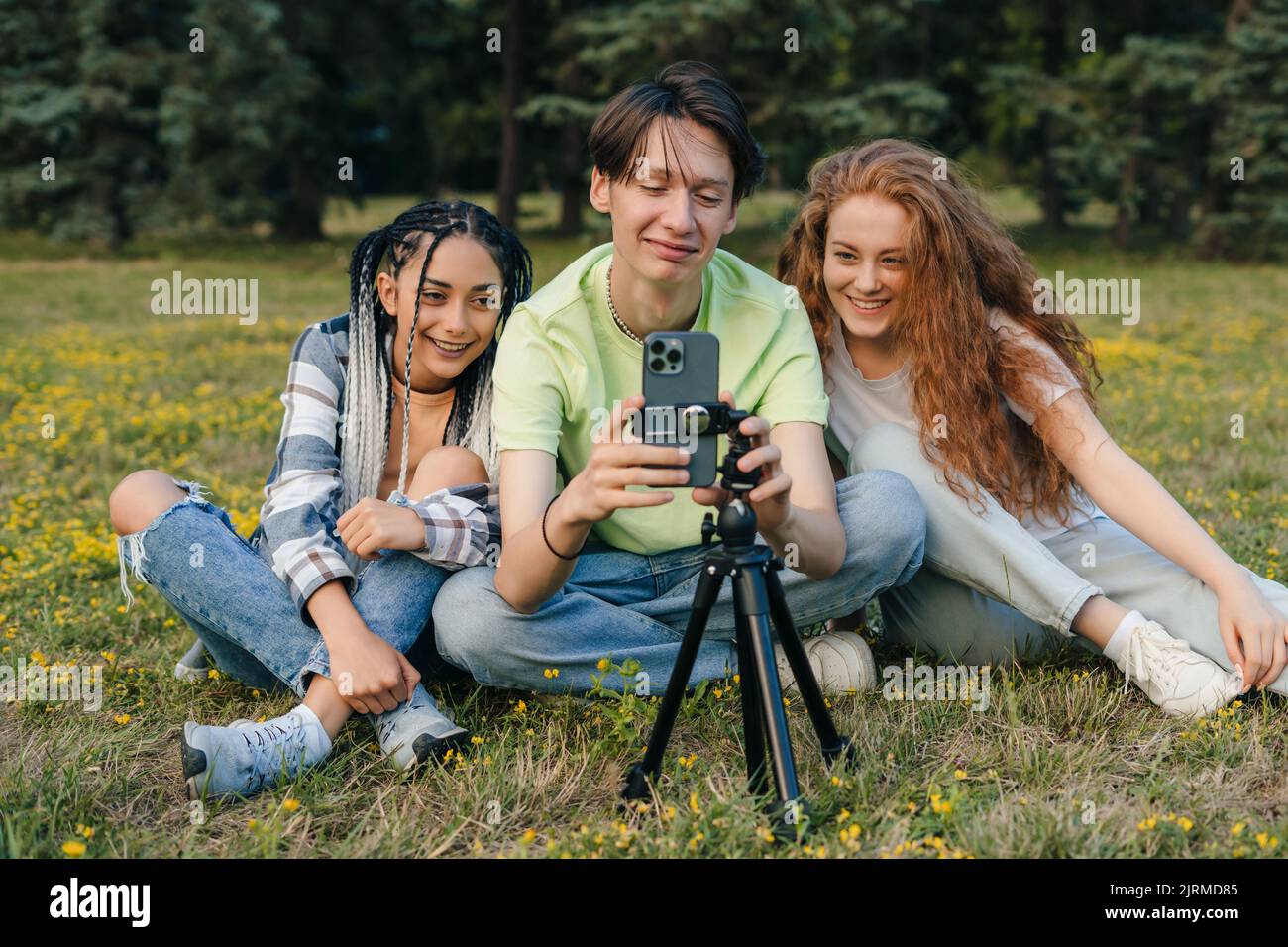 Gruppo di giovani influencer adolescenti seduti sul prato del parco e fare un video live su Internet. L'amicizia e il nuovo concetto di tecnologia in un Foto Stock