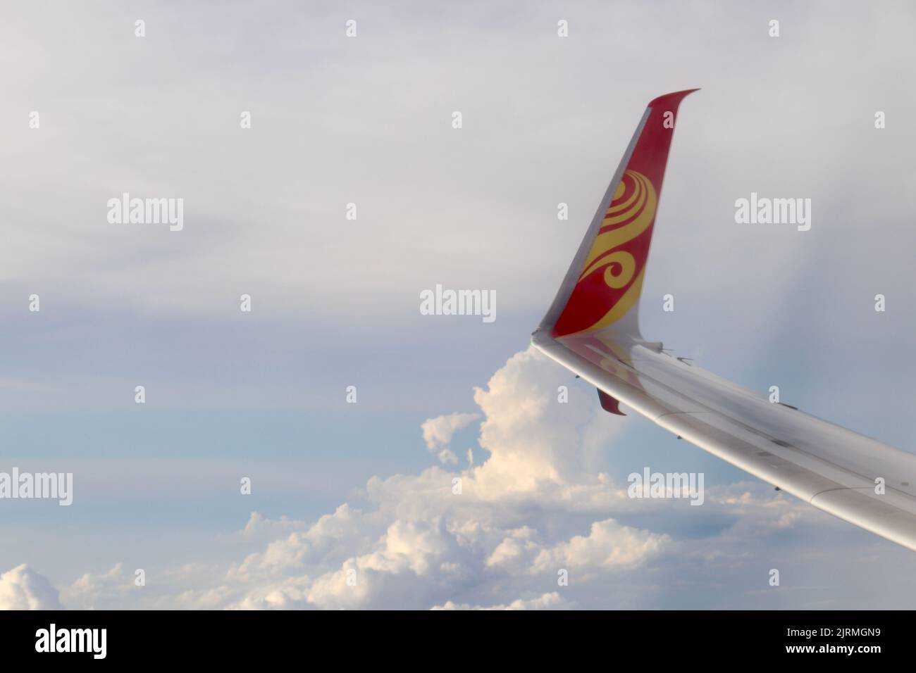 La coda rossa e dorata del Boeing 737-800 di Hainan Airlines nel cielo nuvoloso blu Foto Stock