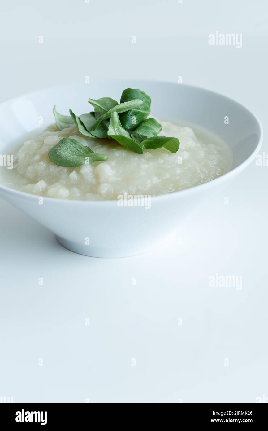Sana zuppa di cavolfiore vegano con erbe in ciotola bianca su tavolo bianco, primo piano Foto Stock