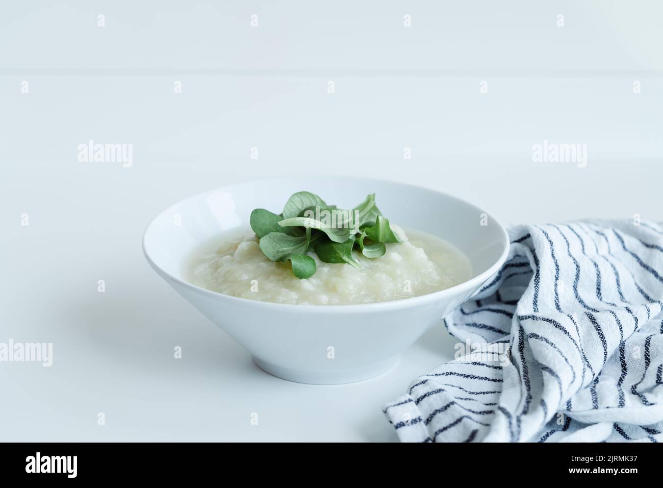 Sana zuppa di cavolfiore vegano con erbe in ciotola bianca su tavolo bianco, primo piano Foto Stock