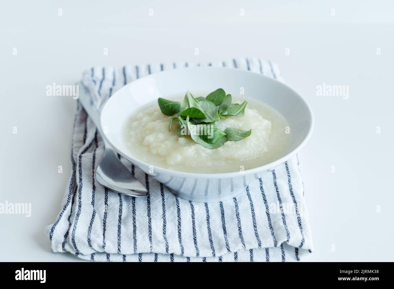 Sana zuppa di cavolfiore vegano con erbe in ciotola bianca su tavolo bianco, primo piano Foto Stock