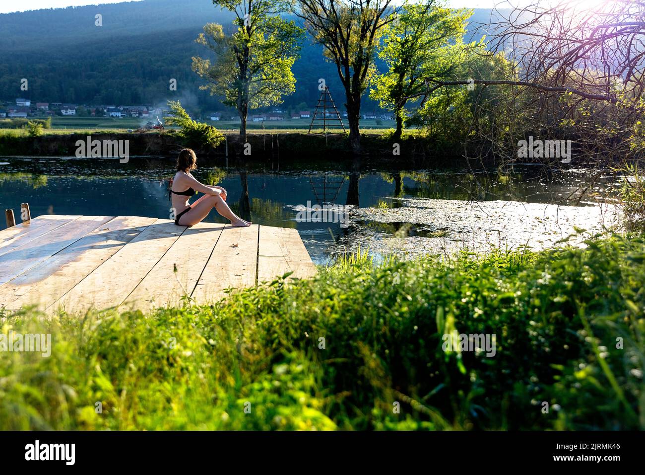 Una turista seduta su un vecchio molo di legno durante una calda serata estiva presso il panoramico fiume Krka nella regione di Dolenjska, in Slovenia. Foto Stock