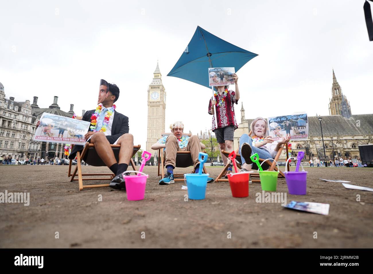 Gli attivisti che indossano maschere di deputati conservatori, tra cui il primo ministro Boris Johnson e i candidati alla leadership Rishi Sunak e Liz Truss, partecipano a una stunt del partito laburista a Parliament Square, Westminster, Mostrare al governo di rilassarsi su una spiaggia con secchi e picche per evidenziare la loro inazione sulle bollette energetiche in vista dell'annuncio del tetto di prezzo Ofgem di venerdì. Data immagine: Giovedì 25 agosto 2022. Foto Stock