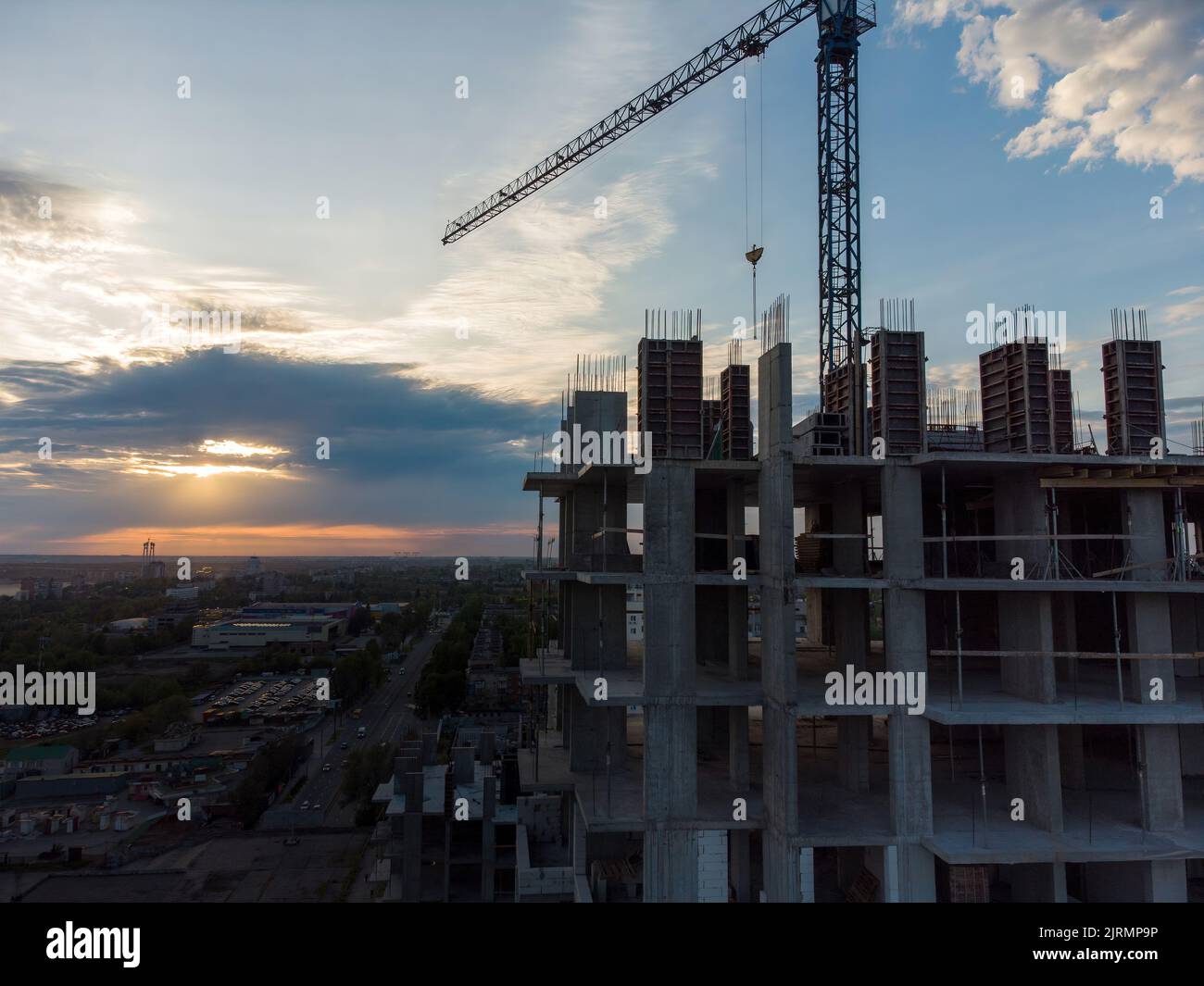 Cantiere con gru sullo sfondo del cielo serale. Gru girevoli a torretta che lavorano al tramonto a sera, edifici sotto Foto Stock