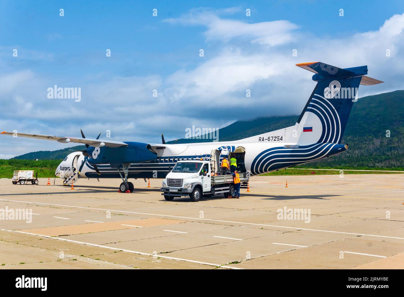 Mendeleevo, Russia - 29 luglio 2022: Scarico bagagli dall'aereo della compagnia aerea Aurora all'aeroporto di Kunashir isola, Mendeleev vulcano è di fronte Foto Stock