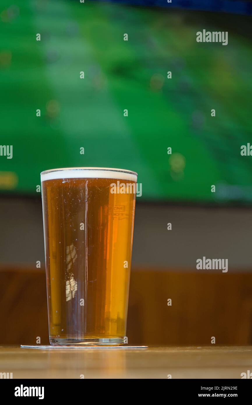 Pinta di birra di fronte A Una televisione che mostra Un calcio, partita di calcio in Una Casa pubblica, Inghilterra UK. Concept Sabato pomeriggio Foto Stock