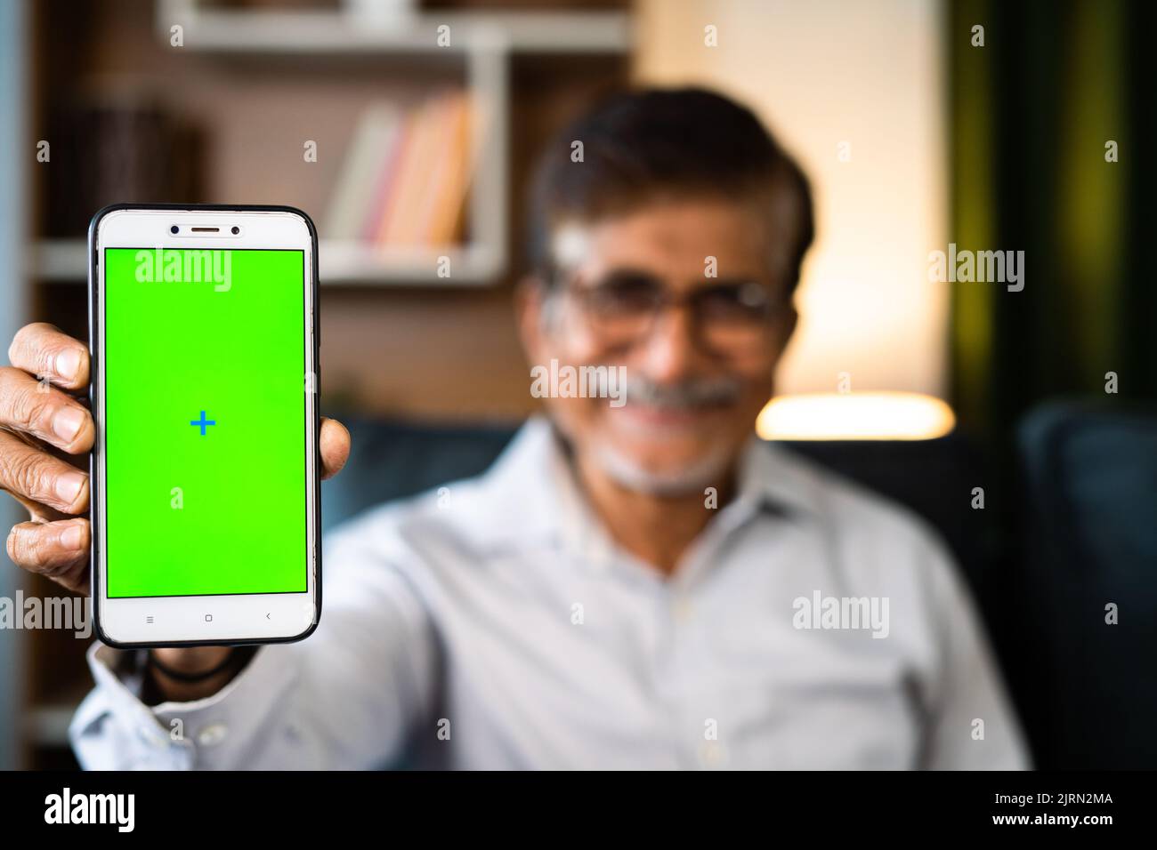 Concentratevi sul telefono cellulare, felice uomo anziano sorridente che mostra il telefono cellulare con schermo verde mentre si siede sul divano a casa con spazio copia - concetto di online Foto Stock