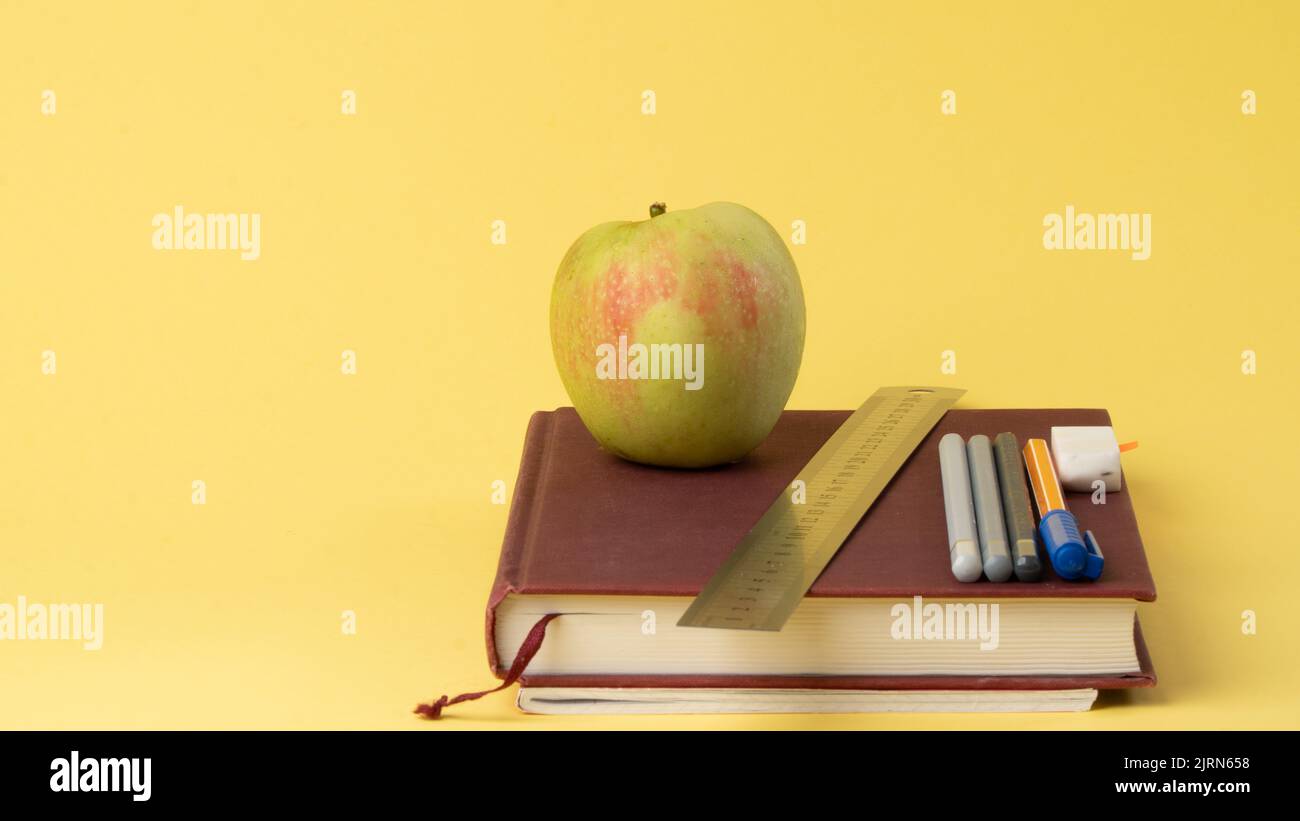 Libri di testo, penne e matite, una mela su sfondo giallo - ritorno a scuola Foto Stock