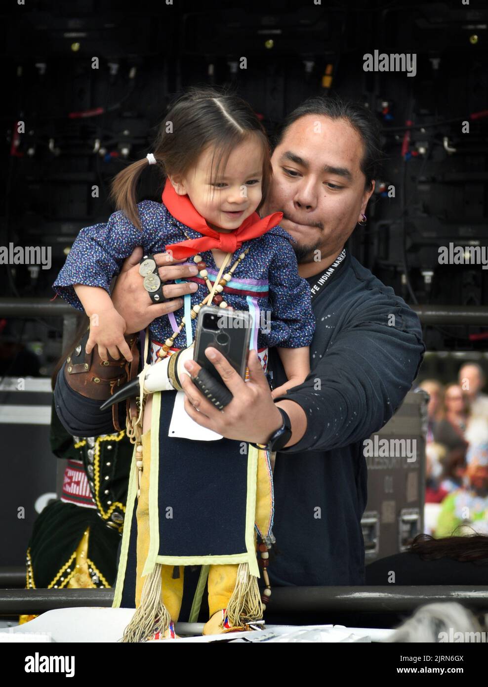 Un uomo nativo americano tiene la sua figlia giovane prima che compete nel concorso di abbigliamento nativo americano al mercato indiano di Santa Fe nel New Mexico. Foto Stock