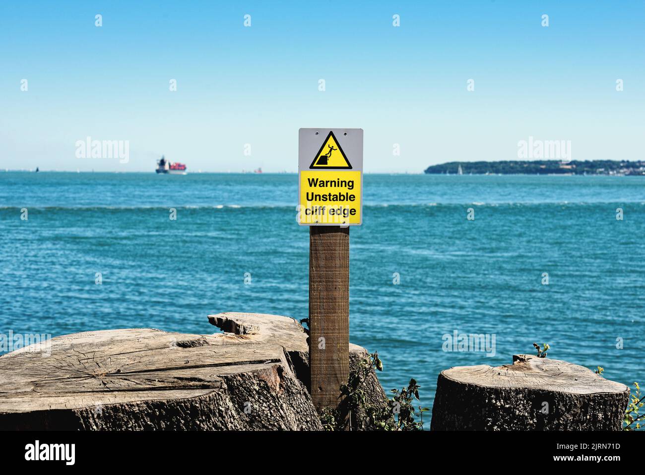 Un segnale di avvertimento giallo che avverte il pubblico sui pericoli di un bordo instabile della scogliera al parco di campagna di Lepe con il Solent nello sfondo Hampshire UK Foto Stock