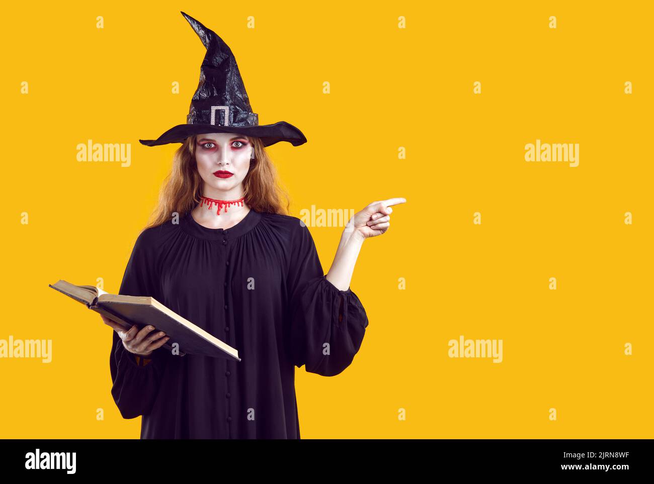 Seria donna creepy in carattere strega che punta con il dito a fianco su sfondo arancione in studio. Foto Stock