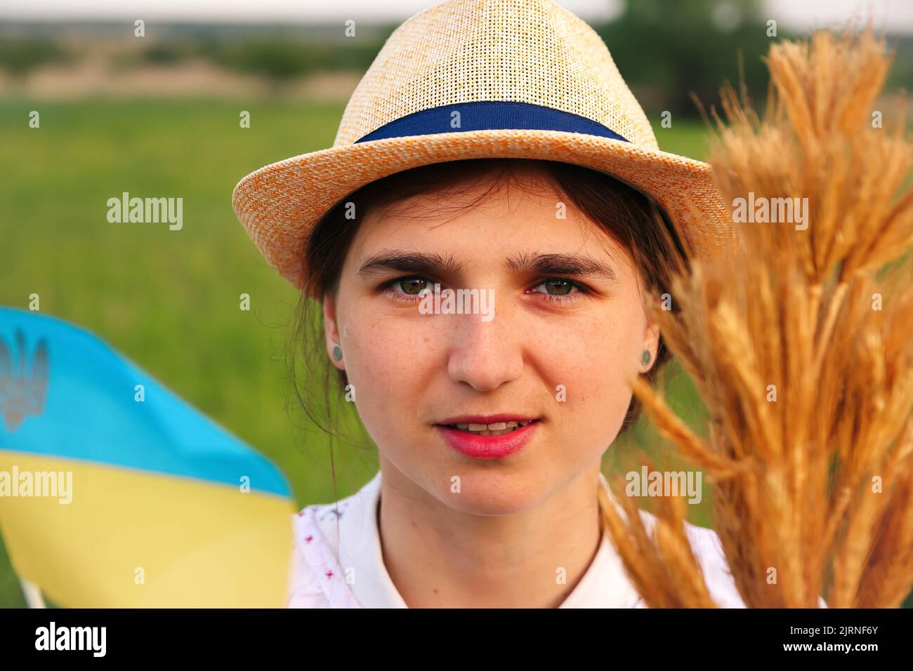 Defocus giovane donna ucraina ritratto. Bouquet di spikelets d'oro maturi di grano legato sul prato natura sfondo. Bandiera Ucraina. Ucraino felice Foto Stock